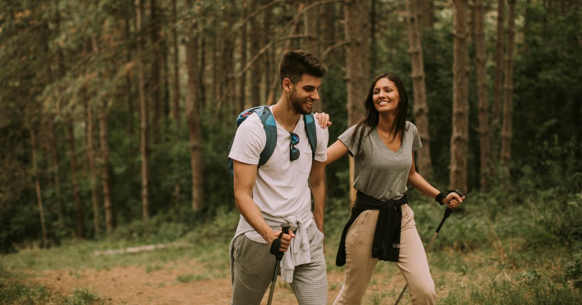 Young man and woman smiling while hiking in the woods with walking sticks.
